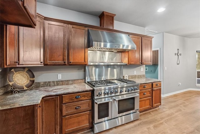 kitchen with baseboards, range with two ovens, light wood-style floors, brown cabinets, and wall chimney range hood