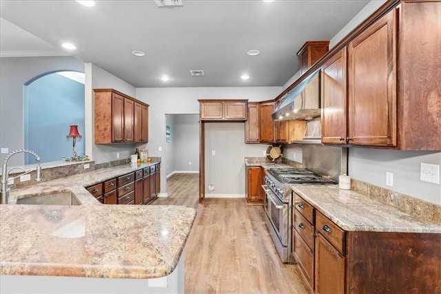 kitchen featuring light stone counters, a sink, light wood-type flooring, high end range, and brown cabinets