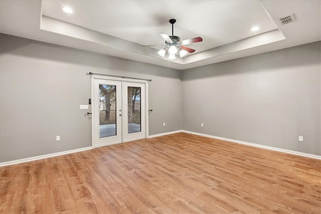 unfurnished room featuring a tray ceiling, light wood-style flooring, and baseboards