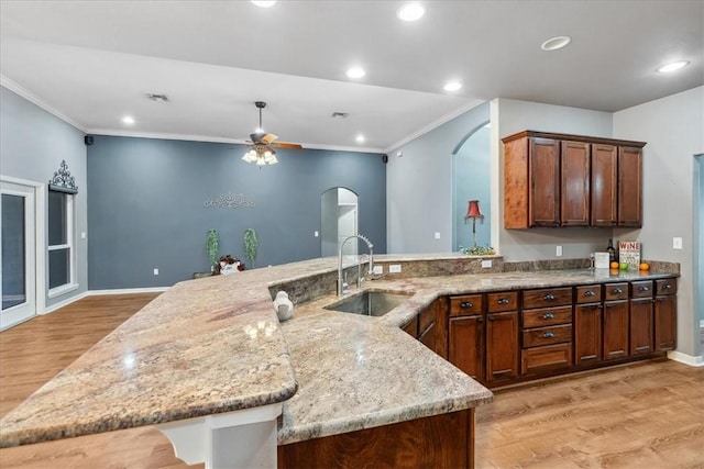 kitchen with light wood-type flooring, arched walkways, light stone counters, and a sink