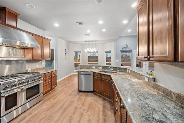 kitchen featuring stainless steel appliances, visible vents, light wood-style floors, a sink, and wall chimney range hood