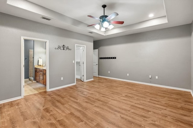 unfurnished bedroom featuring light wood-style floors, a raised ceiling, visible vents, and baseboards