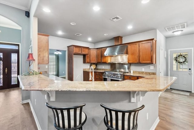 kitchen with range with two ovens, visible vents, light stone counters, and ventilation hood