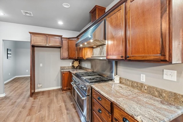 kitchen with brown cabinetry, visible vents, range with two ovens, and light stone counters