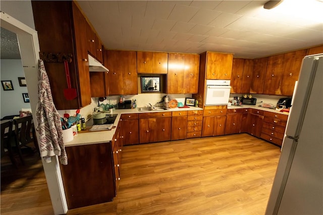 kitchen featuring white appliances, brown cabinetry, light wood-style flooring, light countertops, and under cabinet range hood