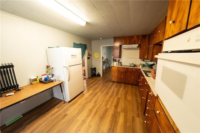 kitchen with white appliances, light wood-style flooring, under cabinet range hood, and light countertops