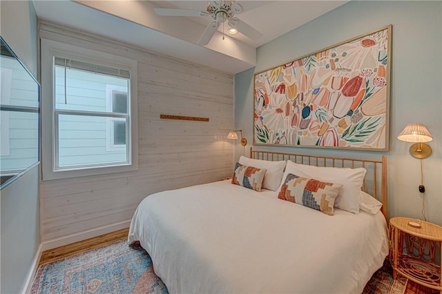 bedroom featuring hardwood / wood-style flooring, ceiling fan, and wood walls