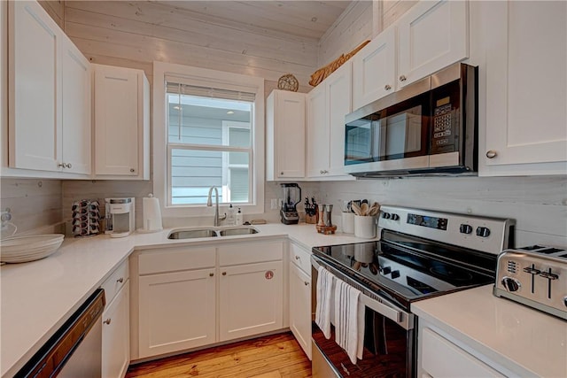 kitchen featuring white cabinetry, stainless steel appliances, wooden walls, and sink