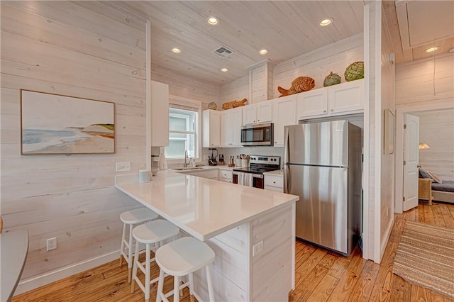 kitchen with wooden walls, appliances with stainless steel finishes, a kitchen breakfast bar, and white cabinets