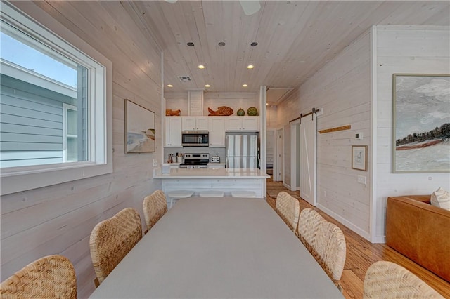 dining space with a barn door, wooden ceiling, wooden walls, and light hardwood / wood-style flooring