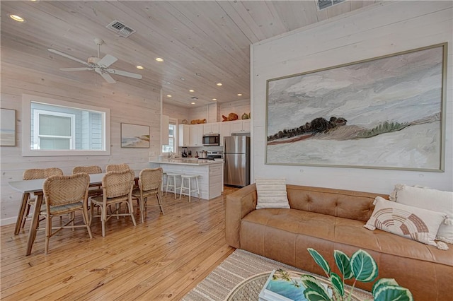 living room featuring wood ceiling, light hardwood / wood-style flooring, wooden walls, and ceiling fan