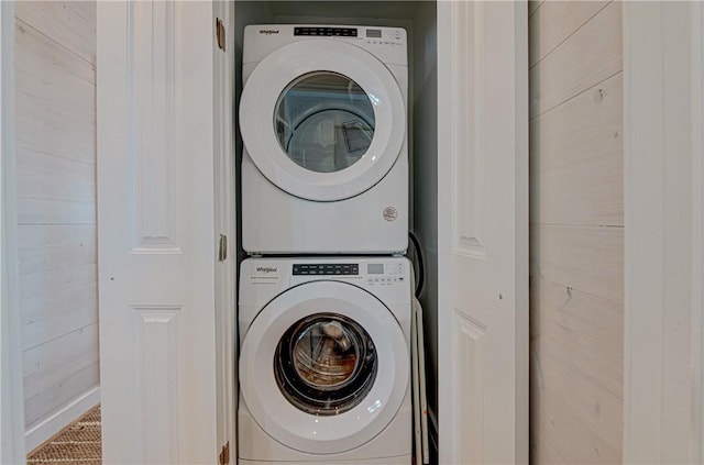 laundry area featuring stacked washer and dryer and wooden walls