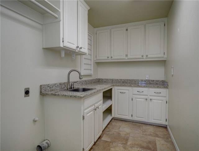 kitchen with baseboards, stone finish floor, light stone countertops, white cabinetry, and a sink