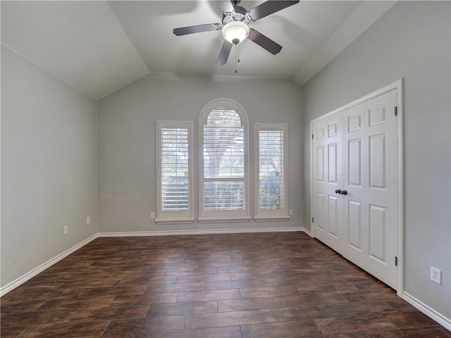 spare room featuring vaulted ceiling, dark wood finished floors, and baseboards