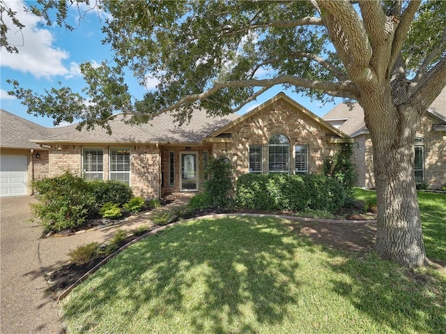 ranch-style home featuring an attached garage, a shingled roof, a front lawn, and brick siding