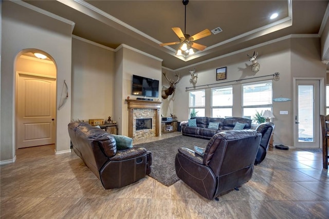 living room featuring ceiling fan, crown molding, a fireplace, and a raised ceiling