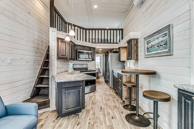 kitchen featuring stainless steel appliances, light hardwood / wood-style floors, dark brown cabinets, pendant lighting, and a high ceiling