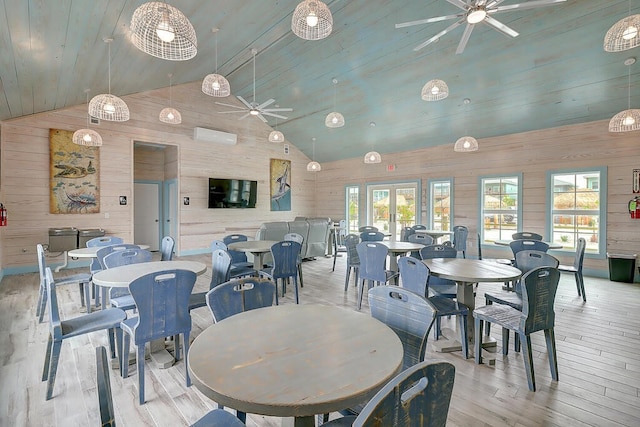 dining room with high vaulted ceiling, a wealth of natural light, wood walls, and light hardwood / wood-style floors