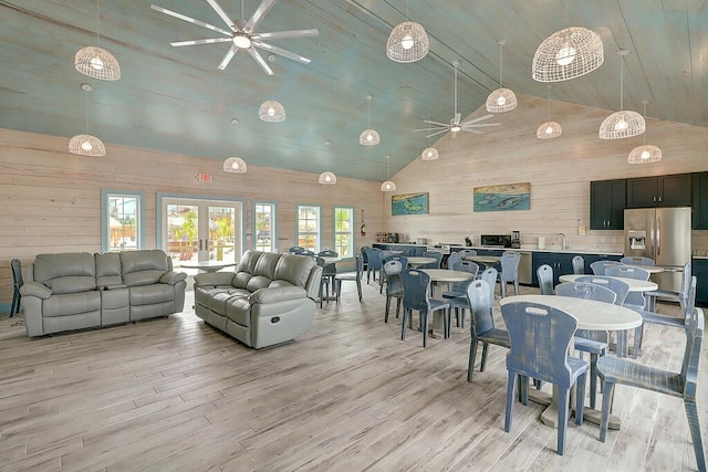 dining space featuring french doors, high vaulted ceiling, wood walls, light hardwood / wood-style floors, and ceiling fan