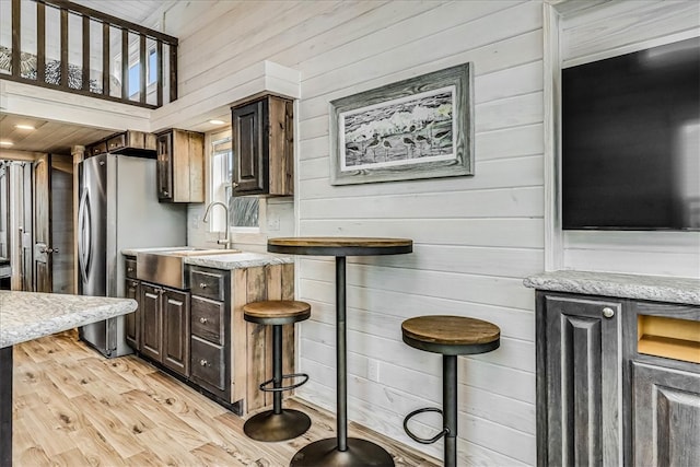 kitchen featuring wood walls, light hardwood / wood-style floors, dark brown cabinets, and sink