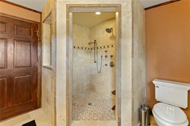 bathroom featuring a tile shower, toilet, and crown molding