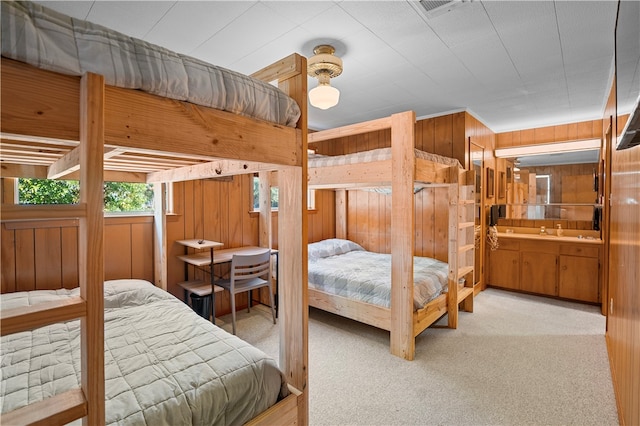 carpeted bedroom featuring wood walls, ensuite bathroom, ceiling fan, and sink