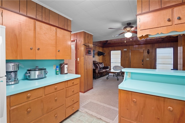 kitchen with wood walls, light carpet, ornamental molding, ceiling fan, and white fridge