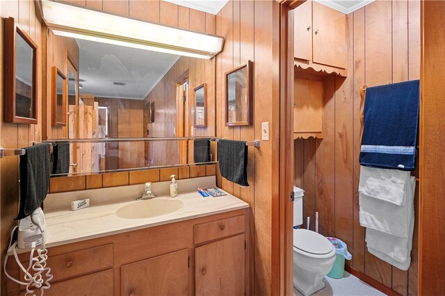 bathroom featuring toilet, wood walls, vanity, and crown molding