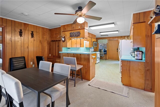 dining area with ornamental molding, wood walls, and ceiling fan