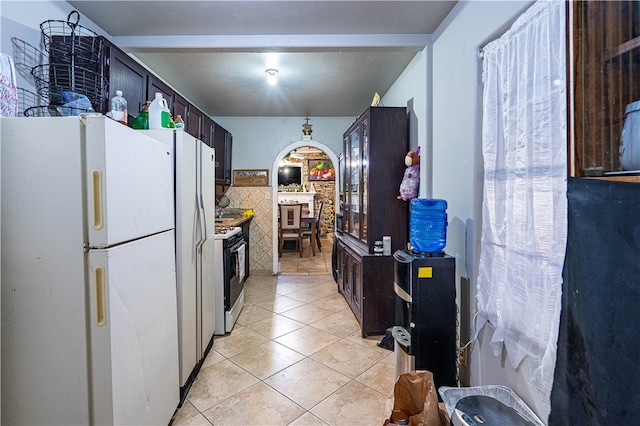 kitchen featuring dark brown cabinetry, light tile patterned flooring, gas range oven, and white refrigerator