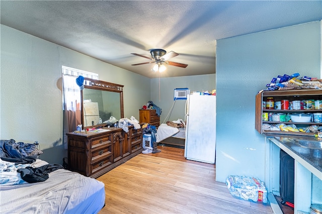 bedroom with light hardwood / wood-style floors, ceiling fan, a textured ceiling, a wall mounted AC, and white fridge