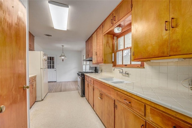 3730 Fort Worth St, Corpus Christi, TX 78411 - kitchen with stainless steel range with gas stovetop, freestanding refrigerator, a sink, brown cabinetry, and under cabinet range hood
