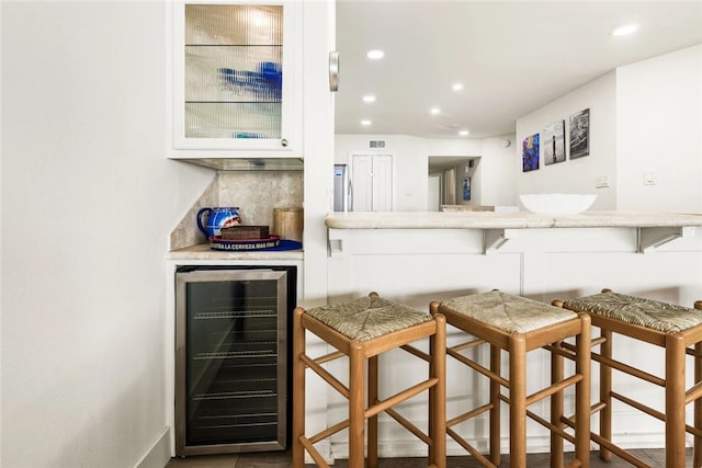 bar with beverage cooler, backsplash, and white cabinets