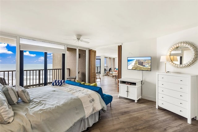 bedroom featuring a water view, a wall of windows, access to exterior, ceiling fan, and dark wood-type flooring