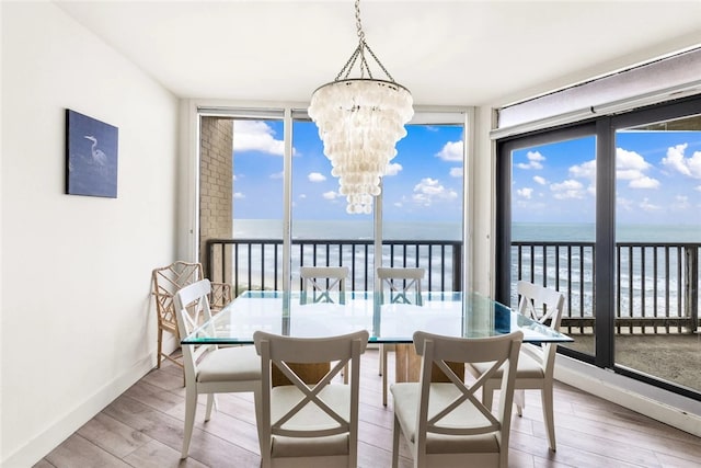 dining area with light wood-type flooring, plenty of natural light, a water view, and a notable chandelier