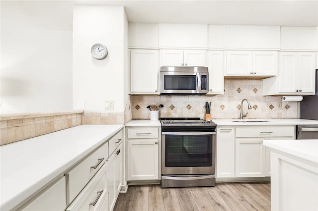 kitchen with sink, appliances with stainless steel finishes, tasteful backsplash, white cabinets, and light wood-type flooring