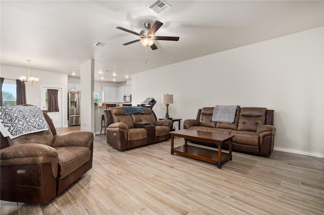 living room featuring ceiling fan with notable chandelier and light wood-type flooring