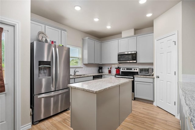 kitchen featuring light stone countertops, sink, a center island, appliances with stainless steel finishes, and light wood-type flooring