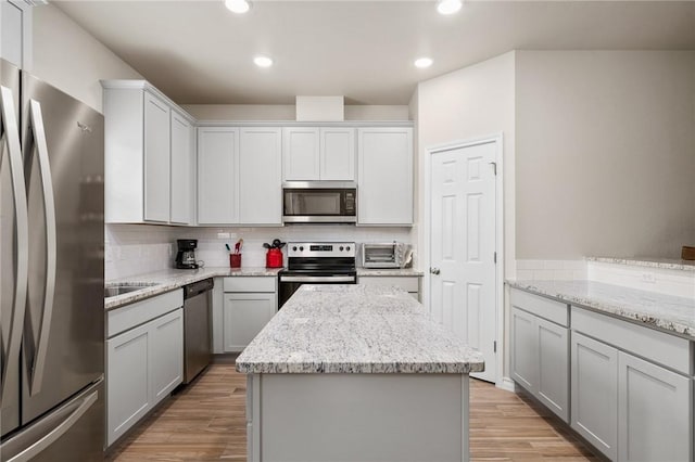 kitchen with light stone countertops, appliances with stainless steel finishes, light hardwood / wood-style floors, and decorative backsplash