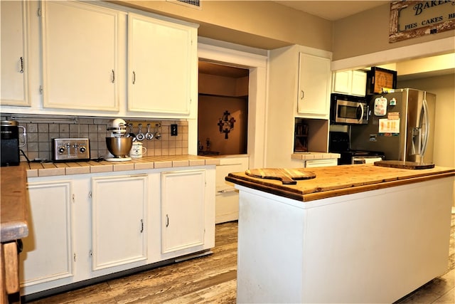 kitchen with tile countertops, hardwood / wood-style flooring, appliances with stainless steel finishes, white cabinets, and decorative backsplash