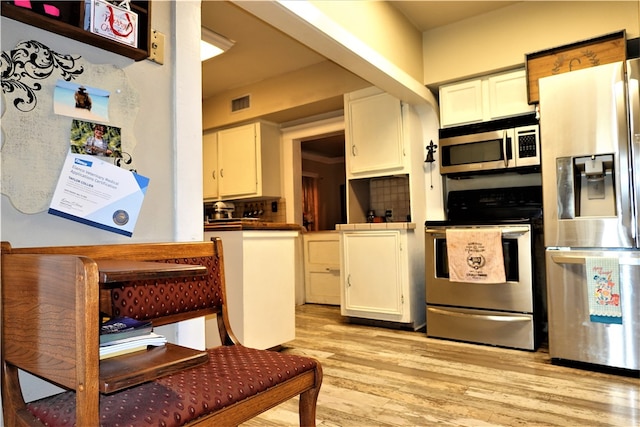 kitchen with white cabinets, light wood-type flooring, appliances with stainless steel finishes, and decorative backsplash