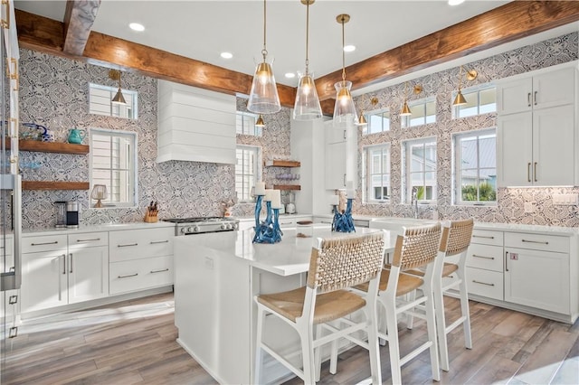 kitchen featuring light hardwood / wood-style flooring, a breakfast bar area, custom range hood, white cabinets, and decorative light fixtures