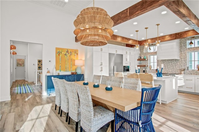 dining area featuring an inviting chandelier, beam ceiling, light hardwood / wood-style flooring, and a towering ceiling