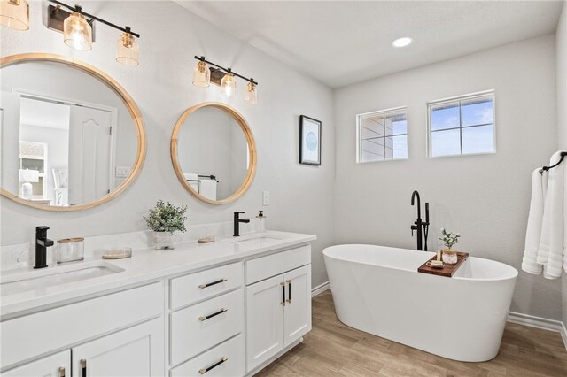 bathroom featuring double vanity, a freestanding tub, wood finished floors, and a sink