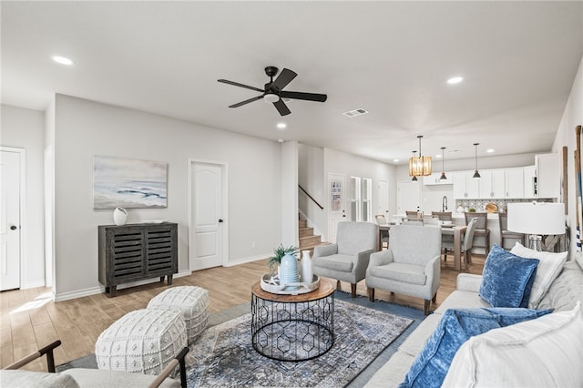 living area with visible vents, light wood-style flooring, a ceiling fan, recessed lighting, and stairs