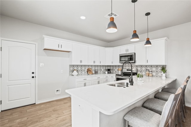 kitchen with tasteful backsplash, visible vents, a peninsula, stainless steel appliances, and white cabinetry