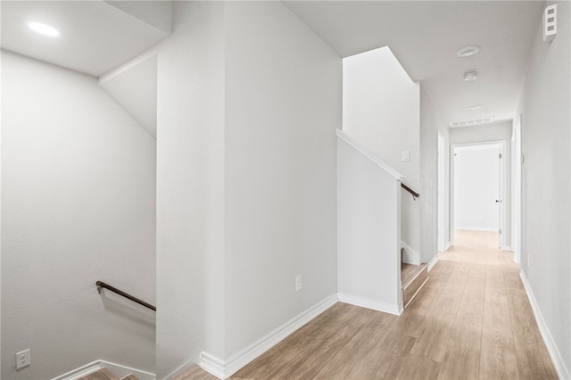 corridor with an upstairs landing, wood finished floors, visible vents, and baseboards