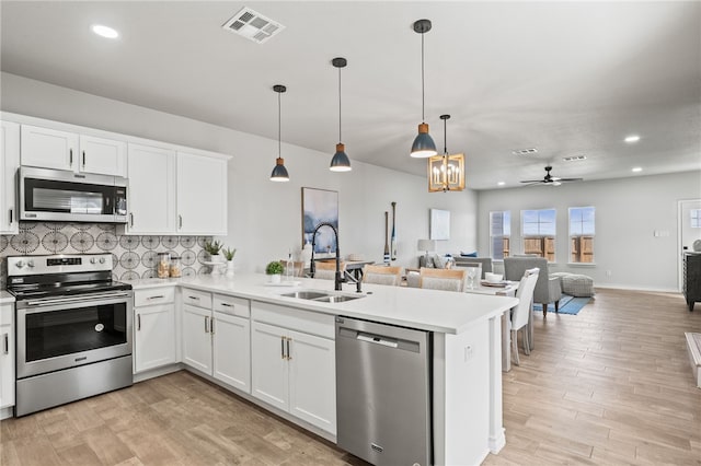 kitchen featuring visible vents, a peninsula, a sink, light countertops, and appliances with stainless steel finishes