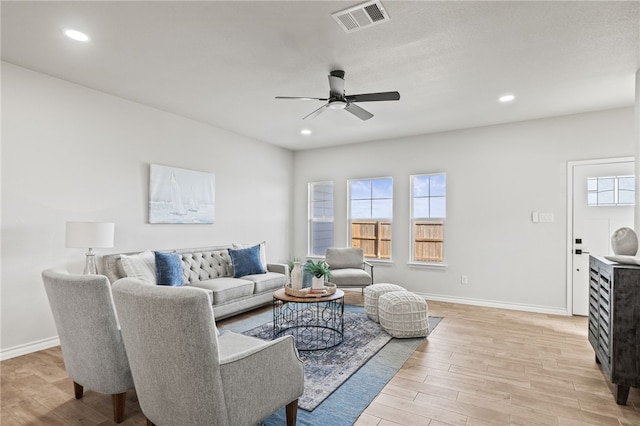 living area featuring a ceiling fan, visible vents, light wood finished floors, and baseboards