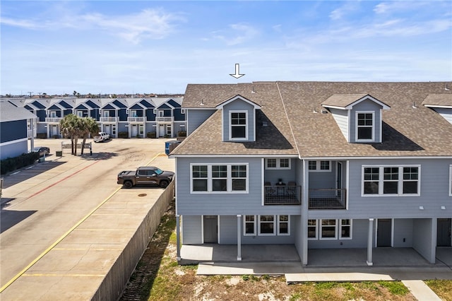 back of house featuring a patio, a balcony, a residential view, and a shingled roof